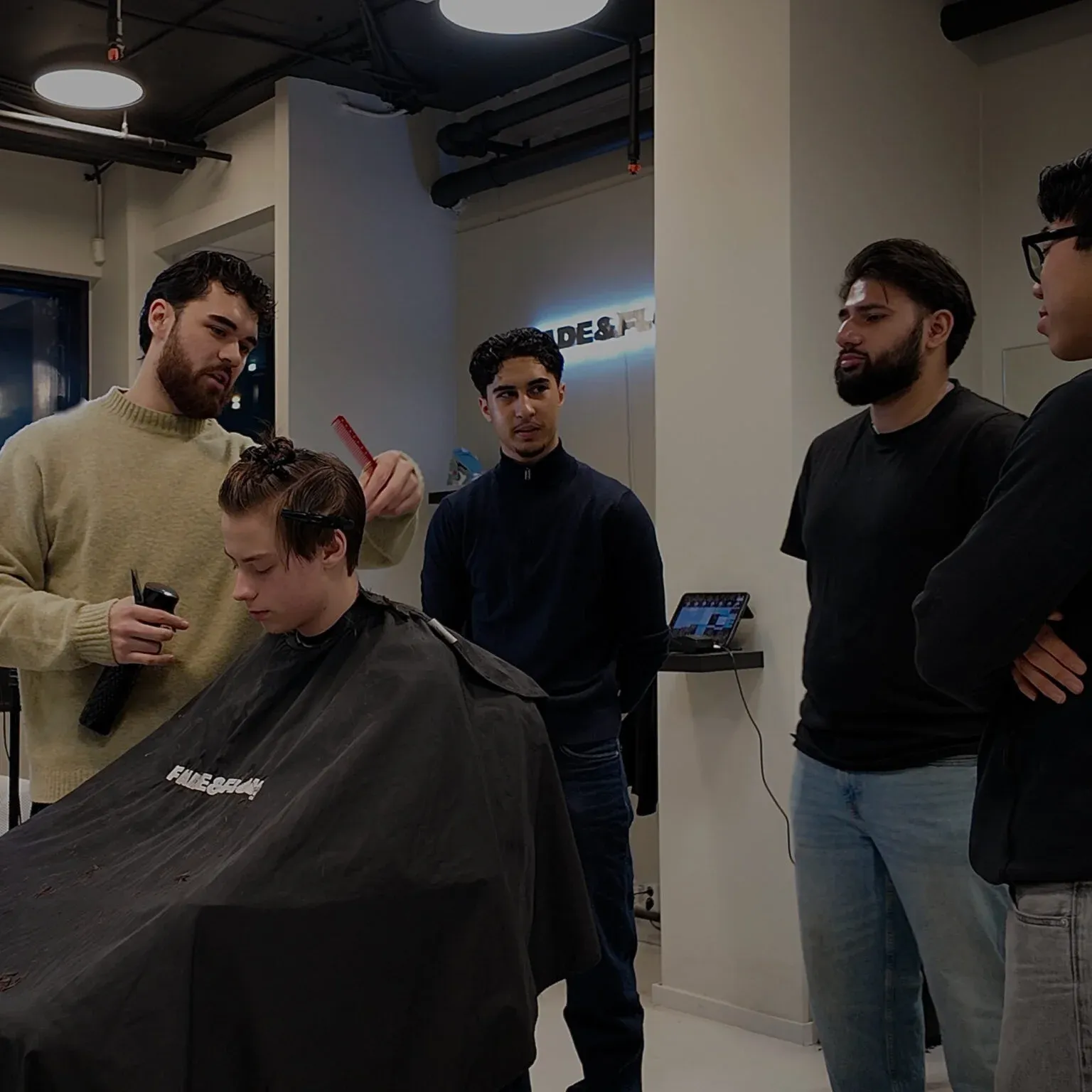 En barber klipper håret til en kunde i FADE&FLOW-lokalet, mens resten av teamet følger med.